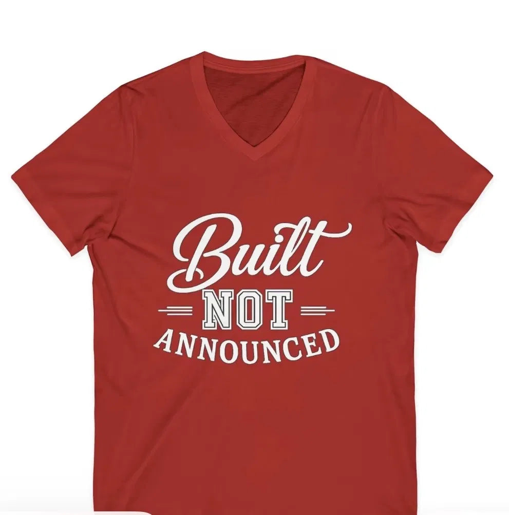 Built, Not Announced red graphic V-neck t-shirt, front view — LUMENORA Studio quote tee